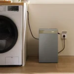 Thumbnail of  De EcoFlow STREAM AC 5000 thuisbatterij aangesloten op een stopcontact in een wasruimte naast een wasmachine.