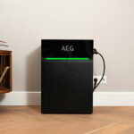 Thumbnail of  Zwarte AEG SOLARCUBE BMS regeleenheid met groene ledverlichting op een houten vloer tegen een witte muur.