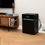 Thumbnail of  Zwarte AEG SolarCube Expand 4.8 kWh module met groene LED-verlichting in een woonkamer naast een houten tv-meubel.