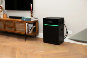 Zwarte AEG SolarCube Expand 4.8 kWh module met groene LED-verlichting in een woonkamer naast een houten tv-meubel.