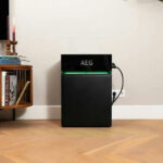 Thumbnail of  Zwarte AEG SolarCube Expand 4.8 kWh uitbreidingsunit met groene verlichting in een woonkamer.