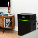Thumbnail of  Zwarte AEG SolarCube Expand unit met groene ledverlichting in een woonkamer naast een houten tv-meubel.
