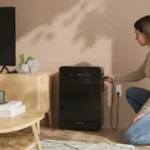 Thumbnail of  Een vrouw sluit een stekker aan op de zwarte Marstek Venus-E 5.12kWh V3.0 thuisbatterij in een woonkamer.